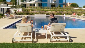 Ein moderner Poolbereich mit Liegestühlen und freiem Blick auf ein mehrstöckiges Gebäude im Hintergrund.