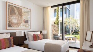 A hotel room with two beds, a large abstract painting, a view of the garden, and a modern building outside.