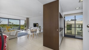 Una sala de estar moderna con sofá, mesa de comedor y sillas, televisor y un ventanal con vistas a zonas verdes.