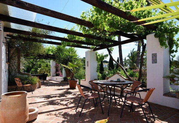 Relax under the shaded pergola, surrounded by lush greenery and comfortable wicker chairs.