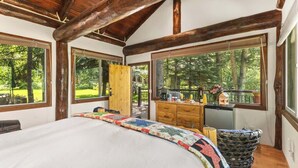 A bedroom with a large bed, wooden beams, a dresser, and a view of the outdoors.