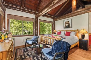 Une chambre confortable avec une tête de lit en bois, un lit recouvert d’une literie rouge et blanche, une table de chevet avec une lampe et une fenêtre donnant sur un paysage verdoyant.