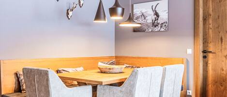 A dining area with a wooden table, grey upholstered chairs, pendant lights, and a wall-mounted deer skull decoration.