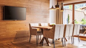 Un espace repas moderne avec un mur en bois, un téléviseur à écran plat et une grande fenêtre donnant sur un paysage verdoyant.