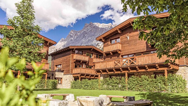Un chalet de montagne doté de balcons en bois et de murs en pierre, situé au pied de sommets enneigés.