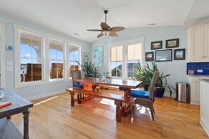 A spacious dining area with a wooden table and benches, large windows, and a ceiling fan.