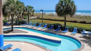 Une piscine aux carreaux bleus, entourée de chaises longues et de palmiers, avec vue sur une plage.