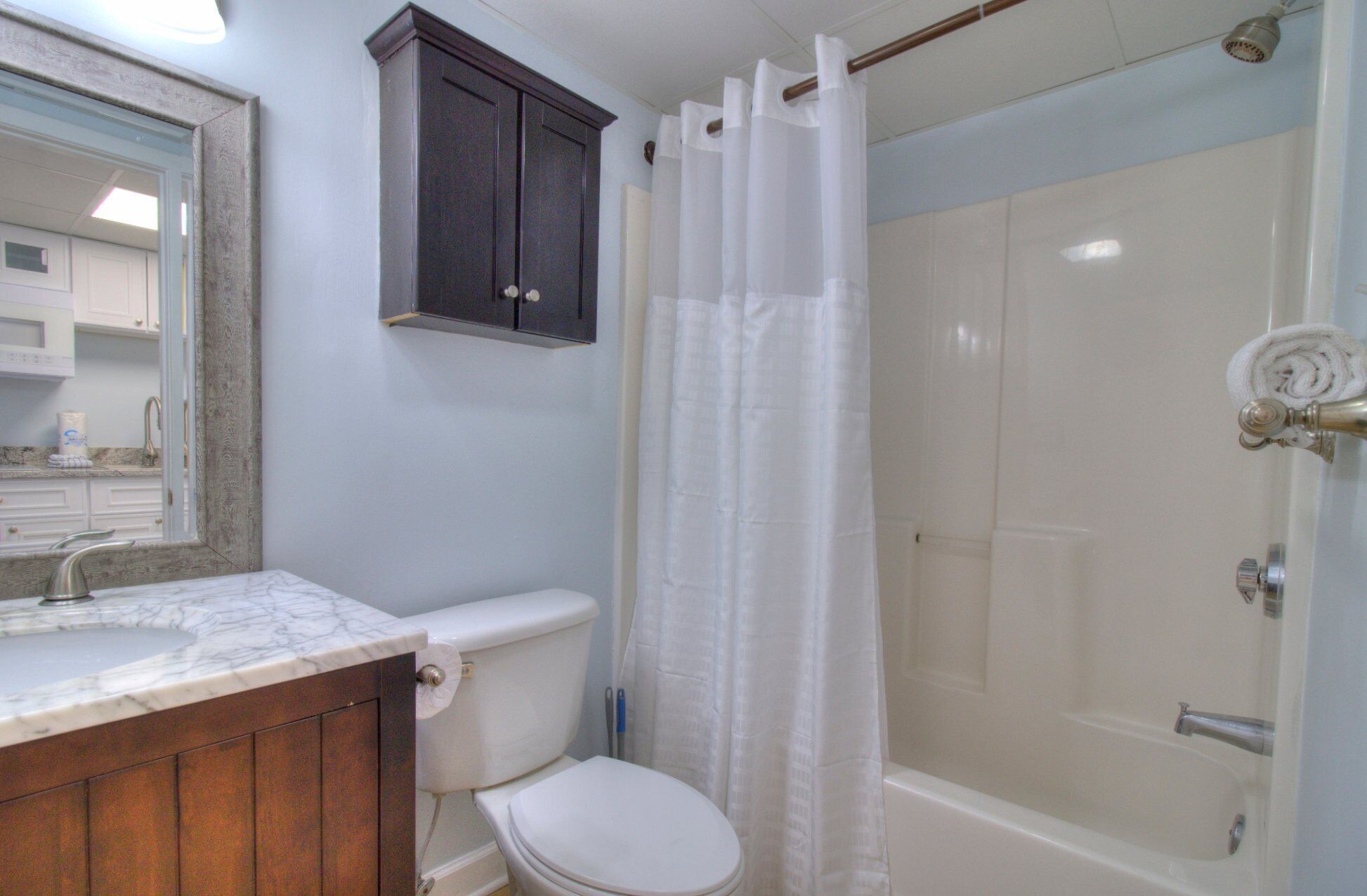 A bathroom with a toilet, a sink, a mirror, a shower with a curtain, and a cabinet.