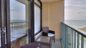 Un balcon agrémenté de meubles en osier, d’une table en verre et offrant une vue sur l’océan.
