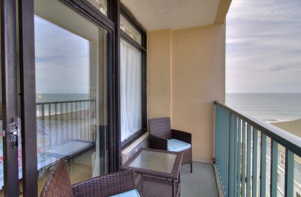 A balcony with wicker furniture, a glass table, and a view of the ocean.