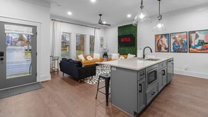 A modern kitchen with a central island, a dining area with a sofa, and a living room with a TV displaying 'NETFLIX'. - NEW! Nash Honky-Tonk w/Game Room, Arcade's, and Pool Table  (Nashville)