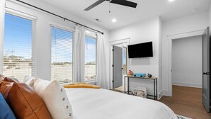 A modern hotel room with a large bed, ceiling fan, TV, and a view of the city. - NEW! Nash Honky-Tonk w/Game Room, Arcade's, and Pool Table  (Nashville)