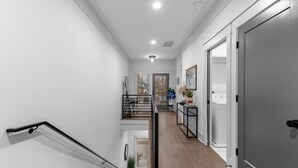 A modern hallway with a wooden floor, white walls, and a staircase with black railings. - NEW! Nash Honky-Tonk w/Game Room, Arcade's, and Pool Table  (Nashville)