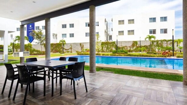 A covered outdoor area with a pool, a dining table with chairs, and a building in the background. - Coto Alejandria Mazatlan/2 Albercas/Cerca del Acuario/Cafe/Equipado/Privado (Mazatlán)