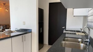 A modern kitchen with a granite countertop, stainless steel sink, and a black refrigerator. - Coto Alejandria Mazatlan/2 Albercas/Cerca del Acuario/Cafe/Equipado/Privado (Mazatlán)
