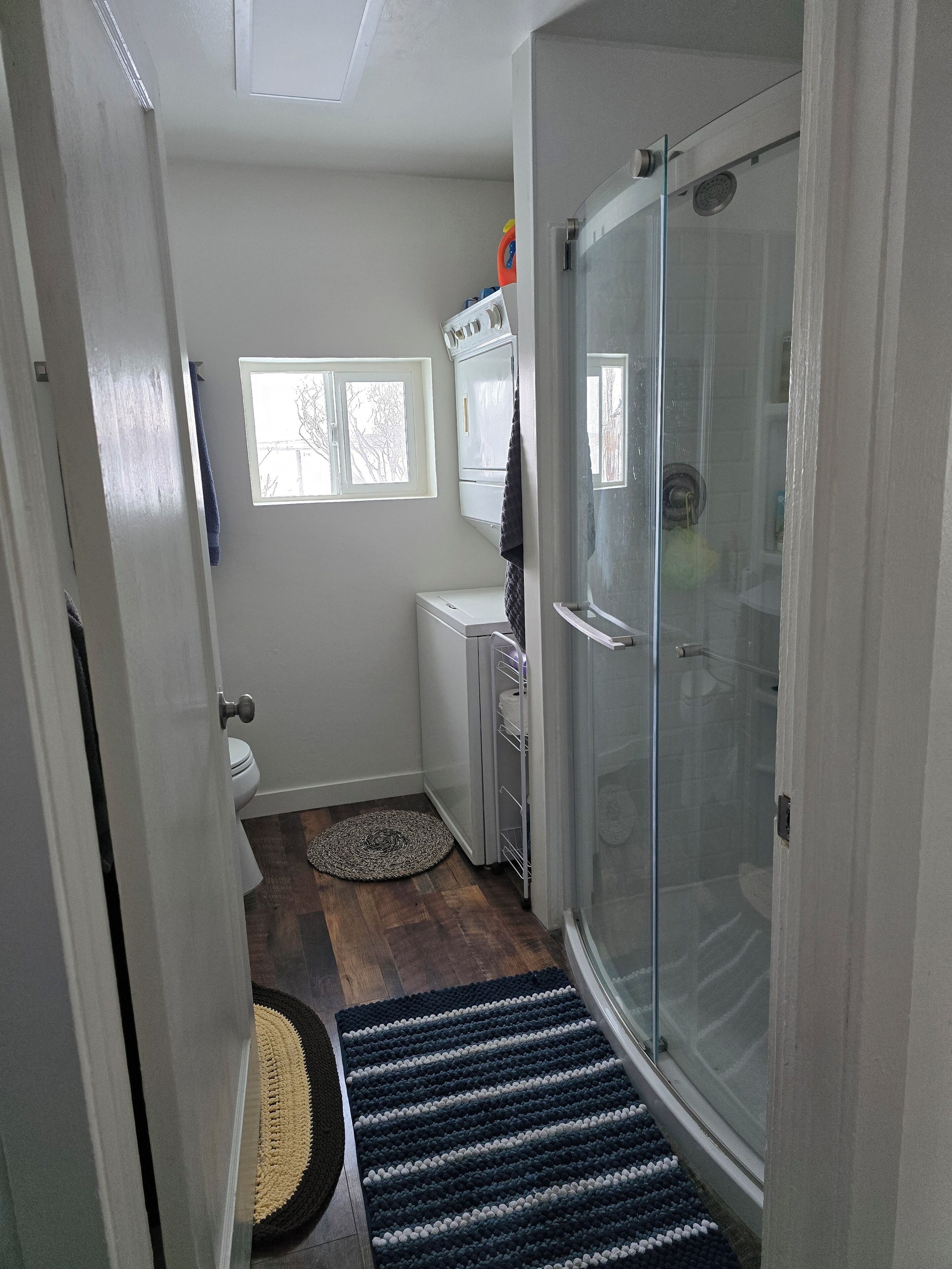 A bathroom with a shower, toilet, and a small window.