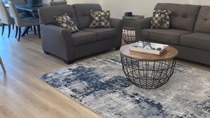 Ein modernes Wohnzimmer mit zwei grauen Sofas, einem runden Couchtisch und einem gemusterten Teppich.