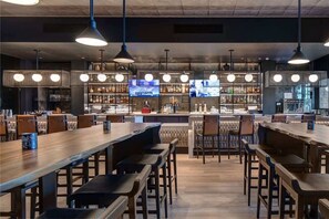 Un espace bar avec des tables et des chaises en bois, un comptoir et des étagères remplies de bouteilles.