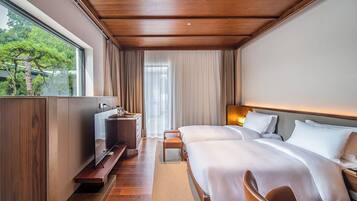 Habitación de hotel moderna con techo de madera, un ventanal con vistas a árboles, dos camas con ropa blanca, una mesita de noche con lámpara y un televisor sobre un mueble de madera.