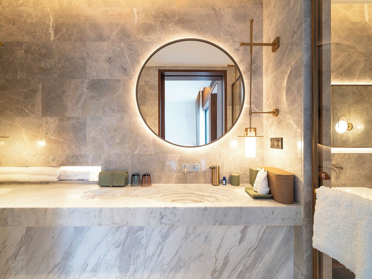 Un baño moderno con encimera de mármol, un espejo redondo y una lámpara en forma de cruz.