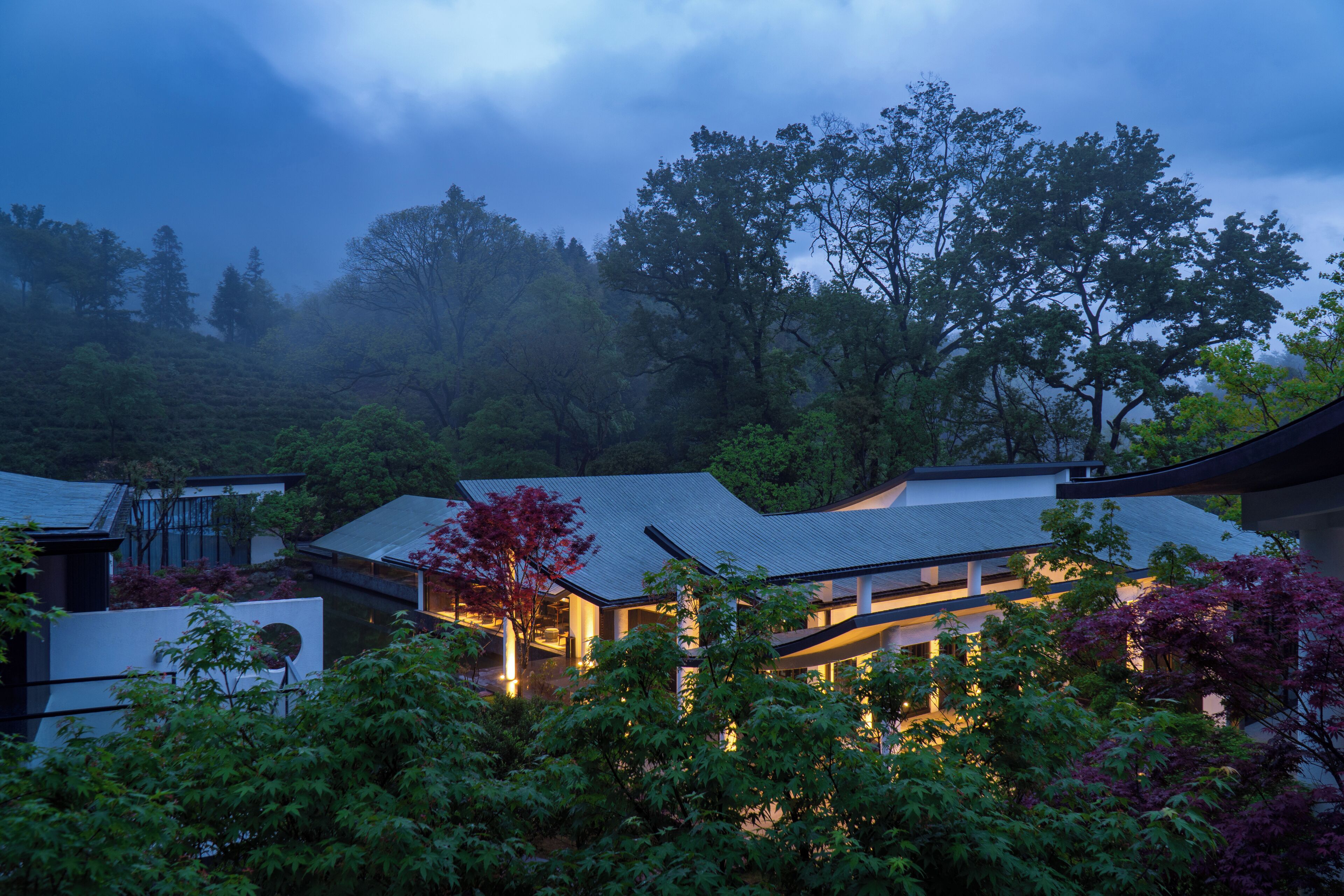 A traditional Japanese house with a sloped roof, surrounded by lush greenery and trees.