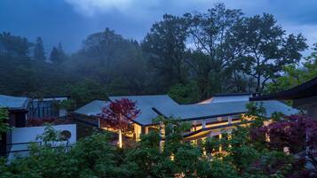 A traditional Japanese house with a sloped roof, surrounded by lush greenery and trees.