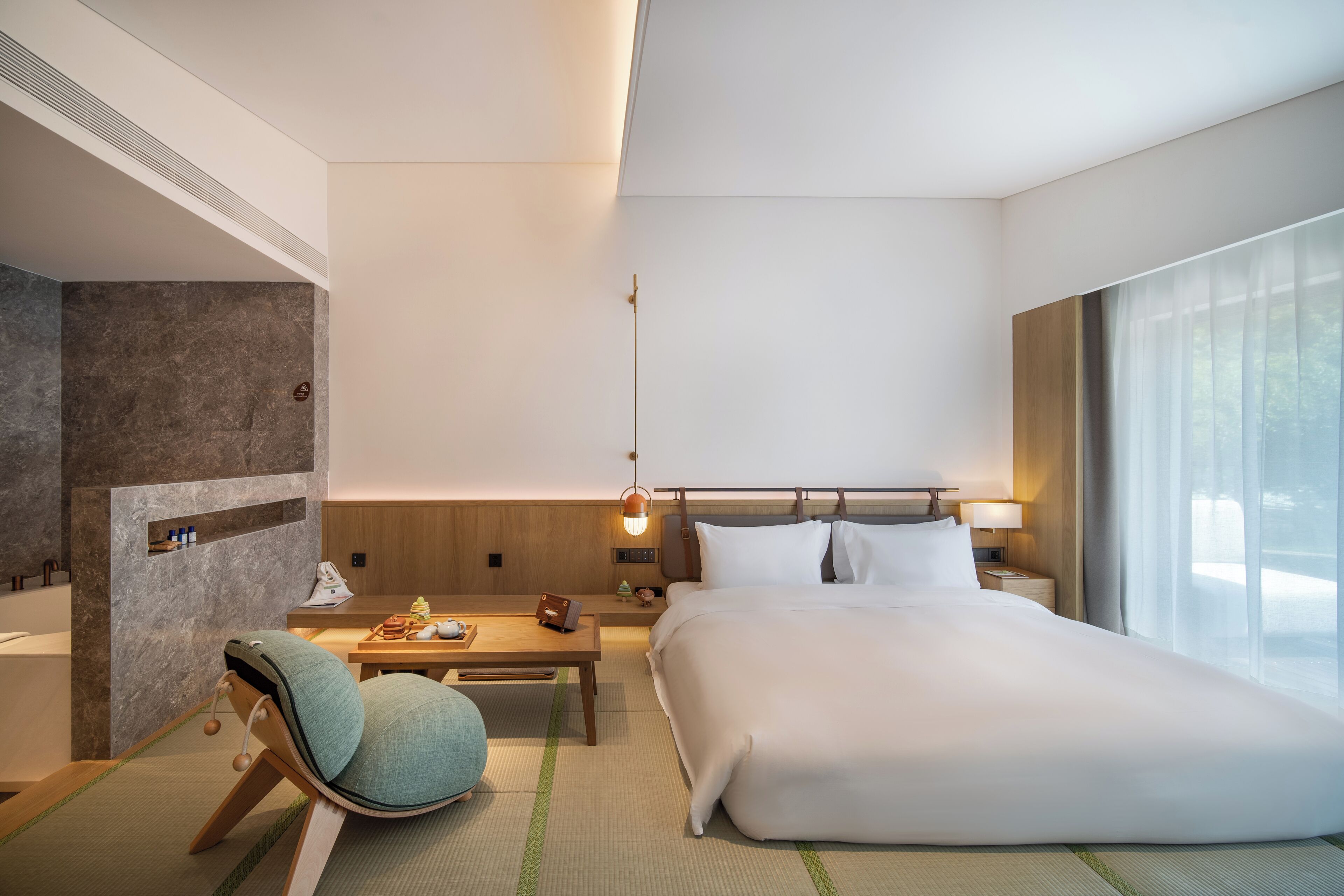 Habitación de hotel moderna con una cama grande, una zona de estar con una silla, una mesita y una mesita de noche.