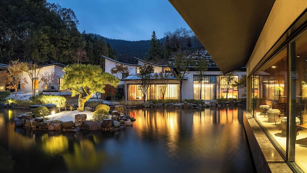 Ein traditionelles japanisches Gebäude mit Teich und Koi-Karpfen, umgeben von Bäumen und Steinen.
