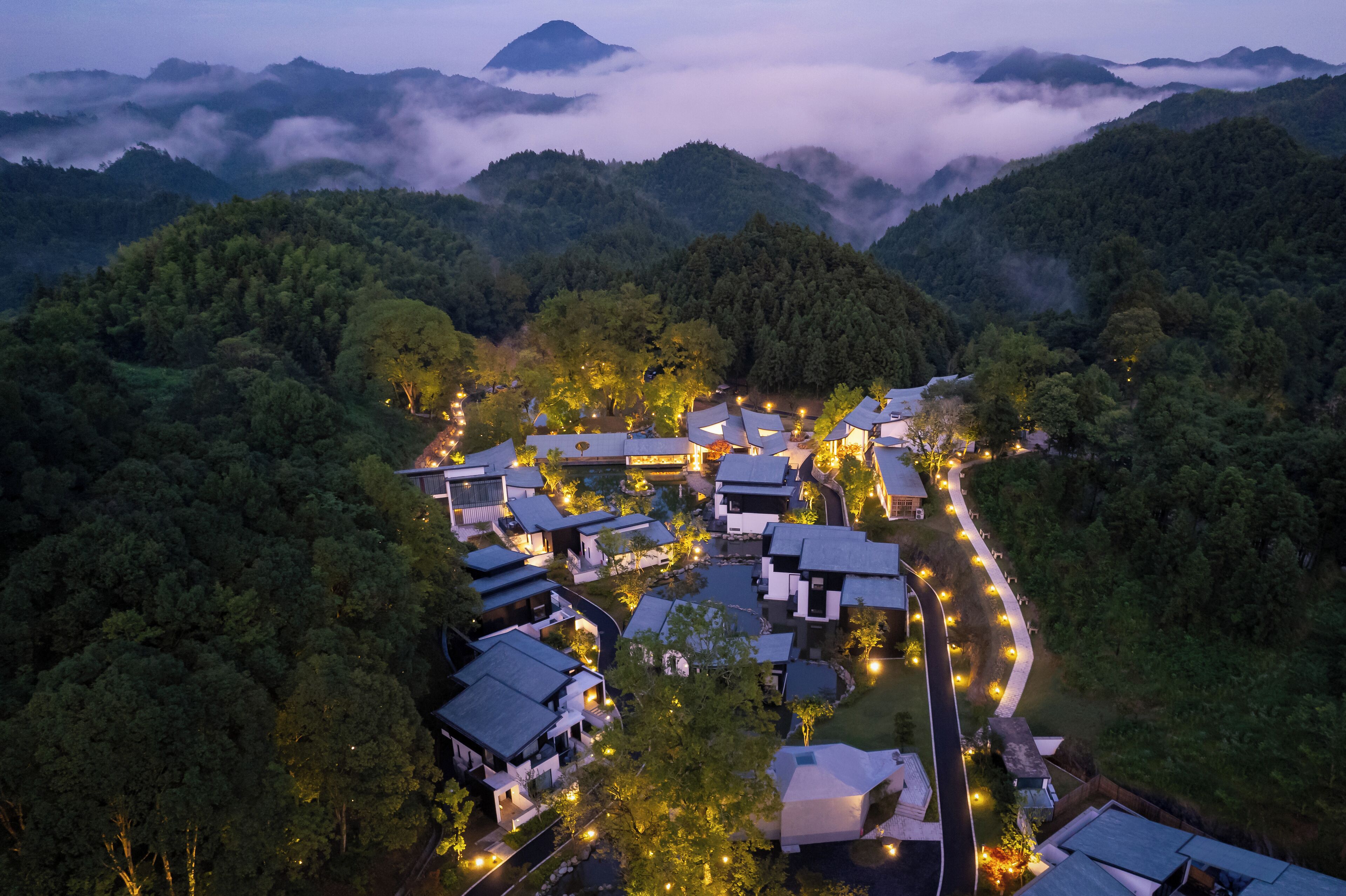 Ett traditionellt japanskt ryokan med flera rum med tatamimattor, en central innergård och utsikt över de omgivande bergen och skogen.