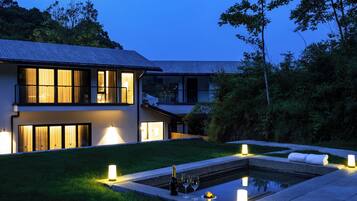 Una casa moderna con piscina, rodeada de césped cuidado y árboles.