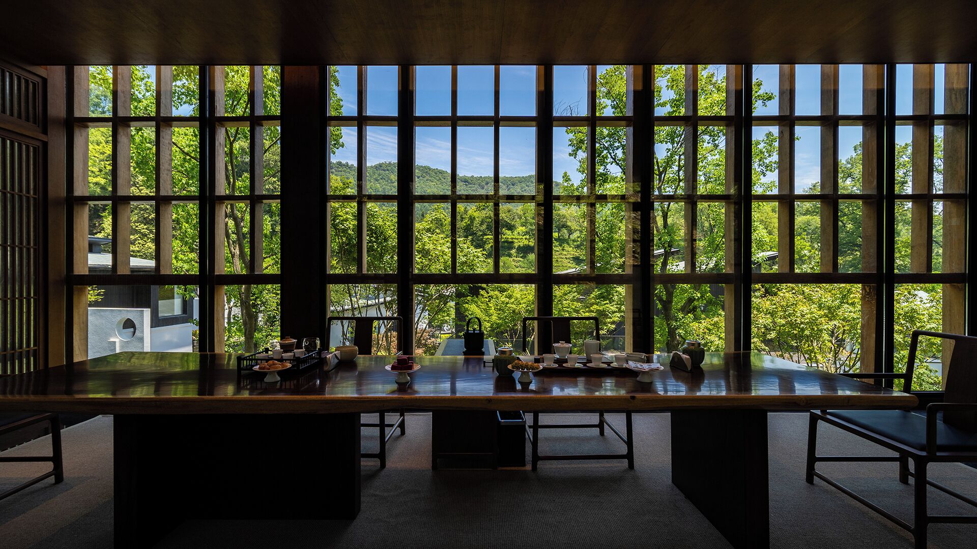 Una habitación con un gran ventanal, una mesa de madera con varios objetos y vistas a un área boscosa.