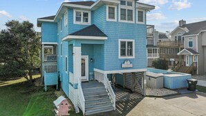 A two-story house with a blue exterior, a front porch, and a small deck. - 1750 - Cool Winds, Corolla Beach House: Private Pool & Hot Tub (Corolla)