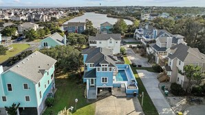A residential area with houses, a swimming pool, and a river in the background. - 1750 - Cool Winds, Corolla Beach House: Private Pool & Hot Tub (Corolla)