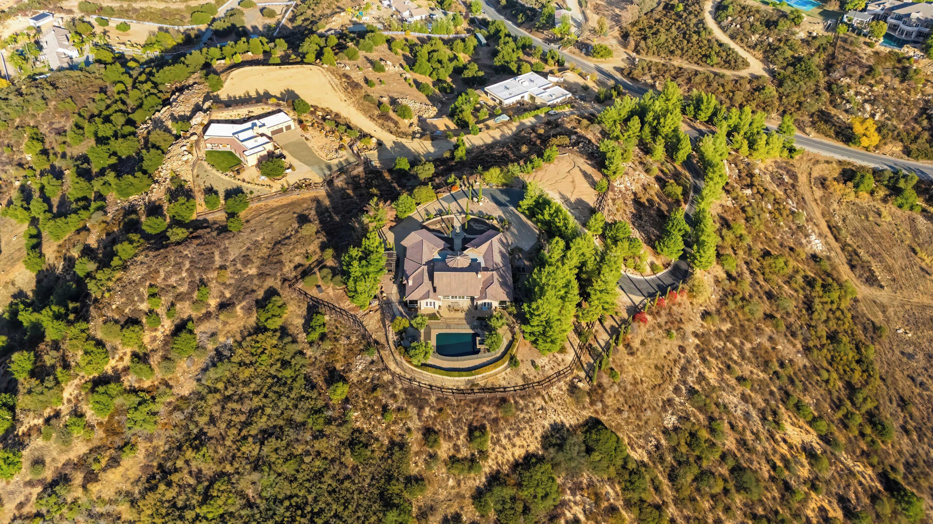 An aerial view of a large estate with a central house, a swimming pool, and surrounding landscaped areas.
