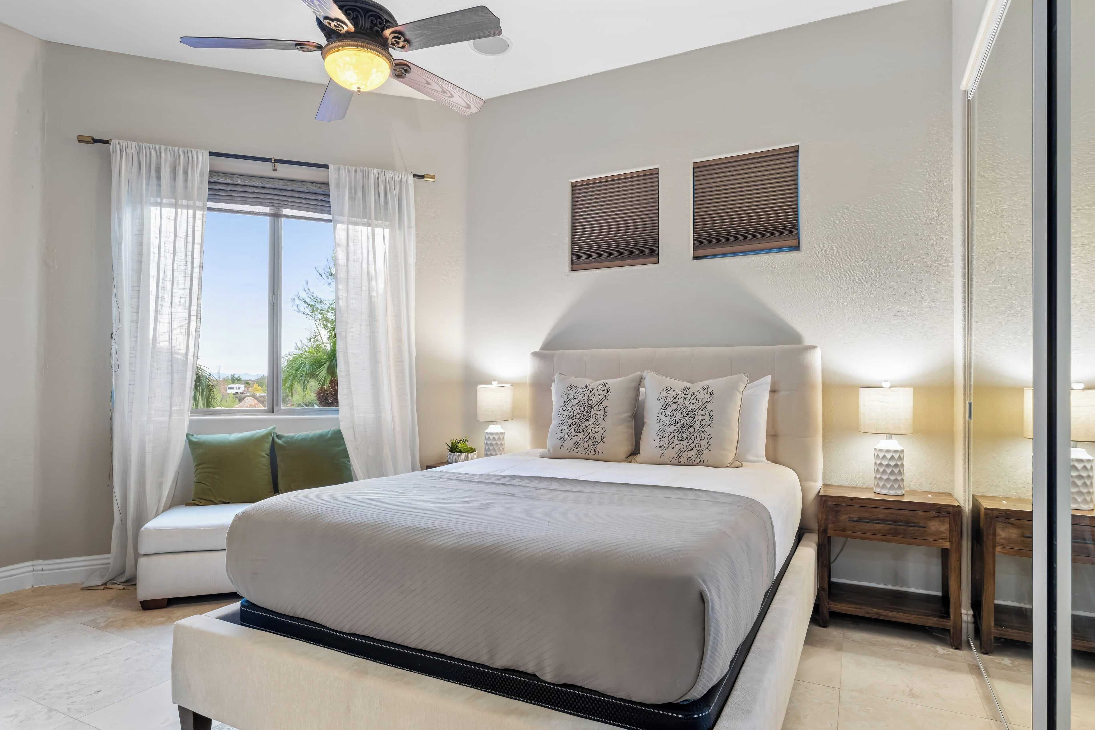 A modern bedroom with a large bed, a ceiling fan, and a view of the outdoors.