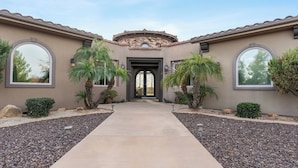 A house with a central entrance, two palm trees, and a pathway leading to the door.