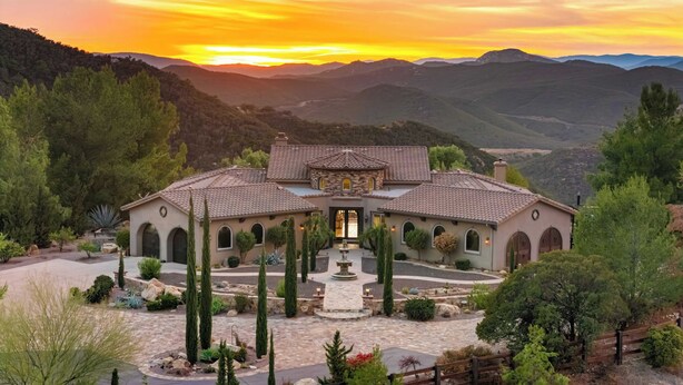 A large, multi-story house with a courtyard, surrounded by mountains and trees.