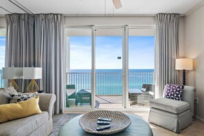 A hotel room with a balcony, a sofa, a chair, and a round table with remotes.