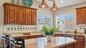 A kitchen with wooden cabinets, granite countertops, and a central island with a potted plant. - The Fritz | Pool + Theater + Games | Sleeps 14 (Glendale)