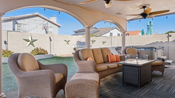 A covered outdoor seating area with wicker furniture, a glass-top table, and ceiling fans. - The Fritz | Pool + Theater + Games | Sleeps 14 (Glendale)
