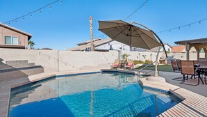 A swimming pool with a curved edge, surrounded by a patio area with chairs and an umbrella. - The Fritz | Pool + Theater + Games | Sleeps 14 (Glendale)