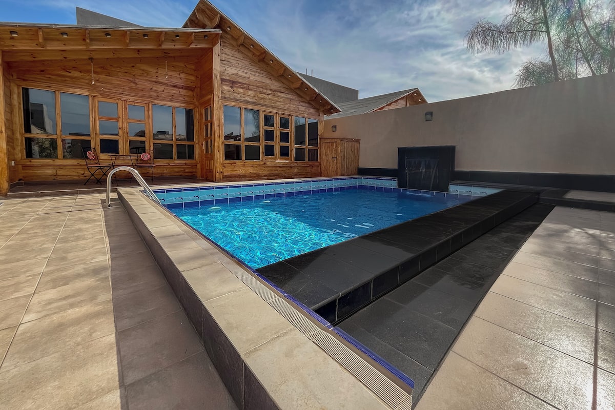 A wooden cabin with a swimming pool, tiled deck, and large windows.