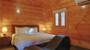 Un dormitori de cabana de fusta amb un llit, làmpades de nit, una finestra i una cadira.