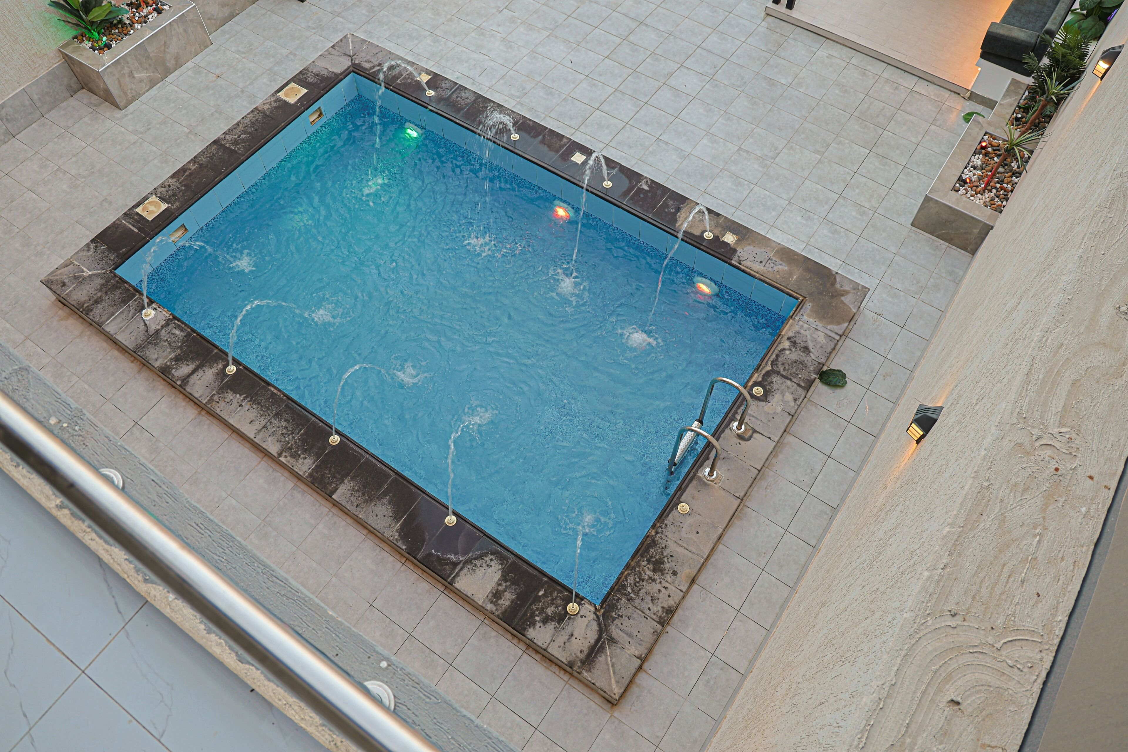 A rectangular pool with multiple water jets, surrounded by tiled flooring and planter boxes with plants.