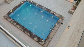 A rectangular pool with multiple water jets, surrounded by tiled flooring and planter boxes with plants.