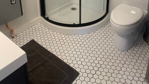 Une salle de bain dotée d’une douche à parois de verre, de toilettes et d’un sol carrelé en forme d’hexagone.