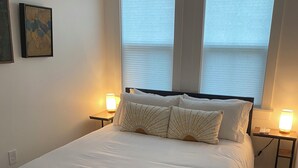 Une chambre à coucher avec un grand lit, deux tables de chevet et une fenêtre avec des stores.