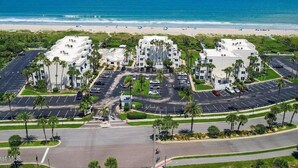 Un hotel frente a la playa con varias construcciones, estacionamiento y vista al océano.