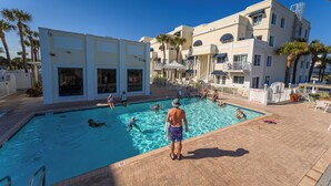 Un área de piscina con varias piscinas, una zona de estar cubierta y un edificio con balcones.