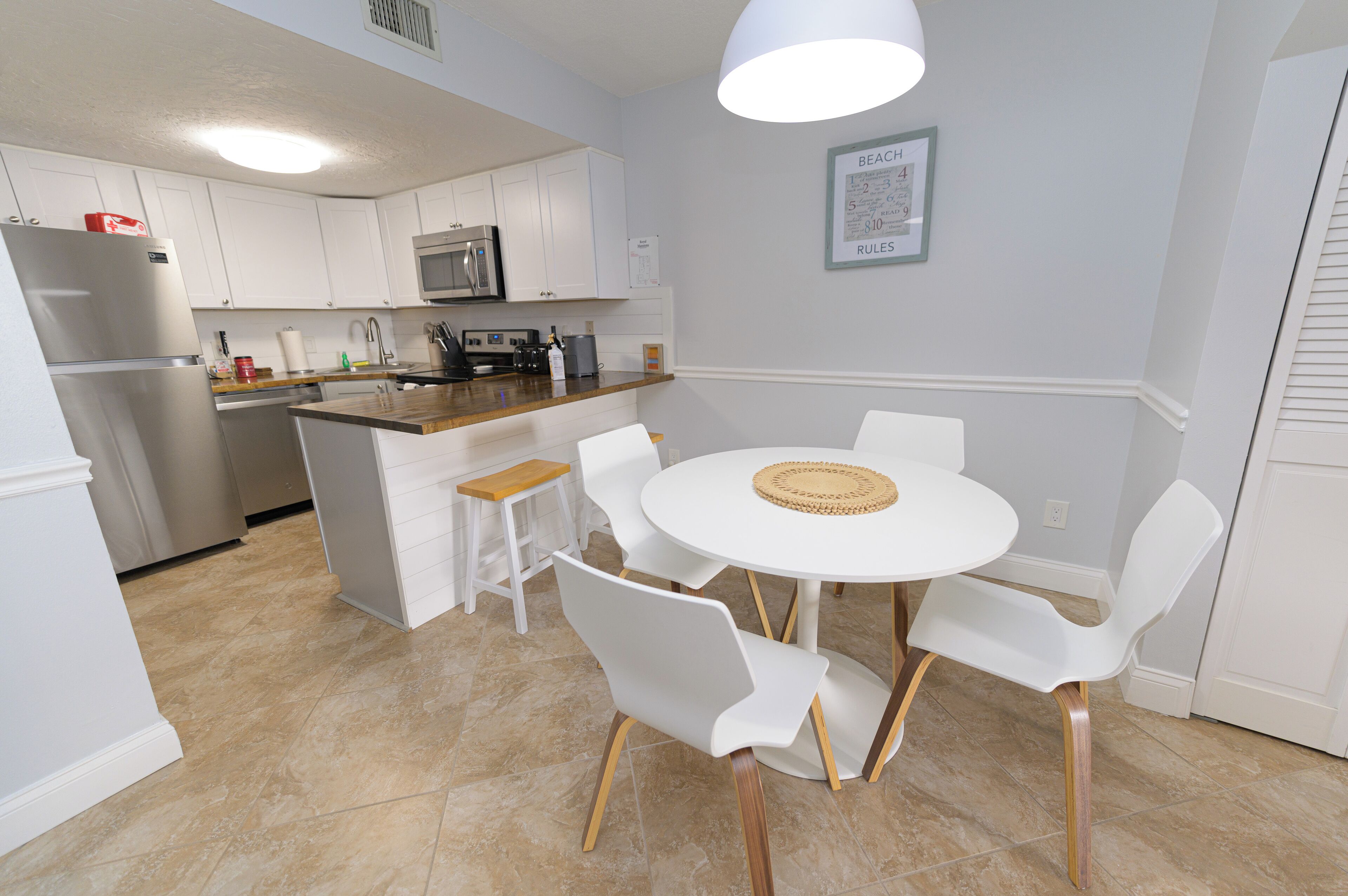 Una cocina moderna con armarios blancos, un refrigerador de acero inoxidable, un microondas e isla de madera con taburetes de bar.